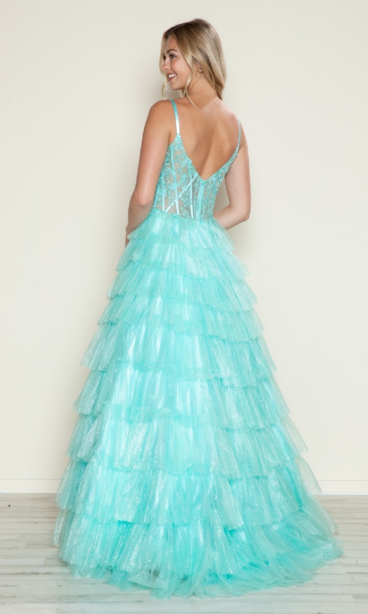 A woman faces away, wearing the Long Prom Dress: Poly USA 9608—a light blue gown featuring a tiered skirt, sheer back, ruffles, and delicate spaghetti straps.